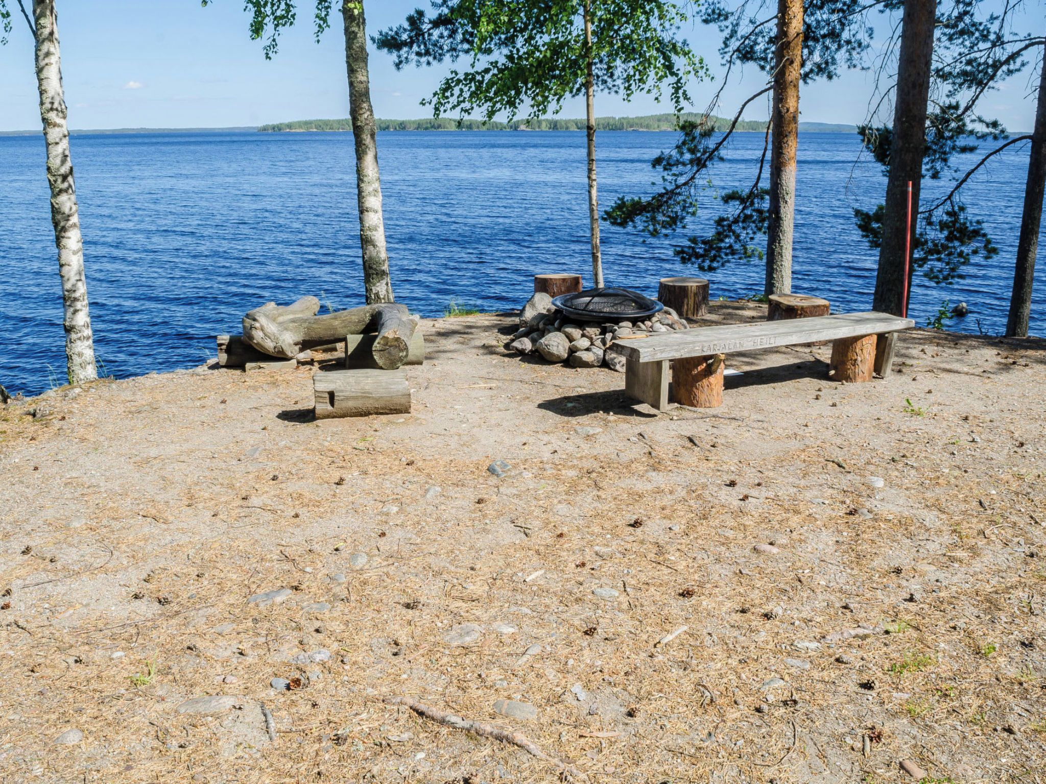 A lakeside campsite with a bench, a fire pit, and a pile of logs.