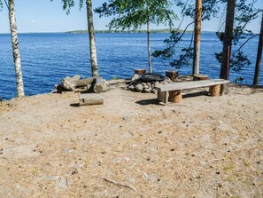 Un campamento junto al lago con un banco, una fogata y una pila de leña.