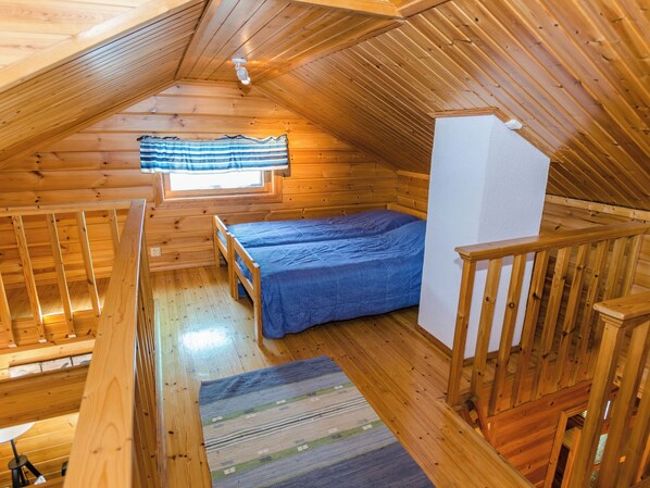 Uma cabana de madeira com quarto no mezanino, uma pequena janela com cortina listrada e escada de madeira.