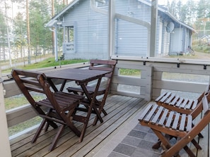 A wooden deck with a table and chairs, a covered area with a railing, and a view of a blue building in the background. - Karjalan heili 17 by Interhome (Lieksa)