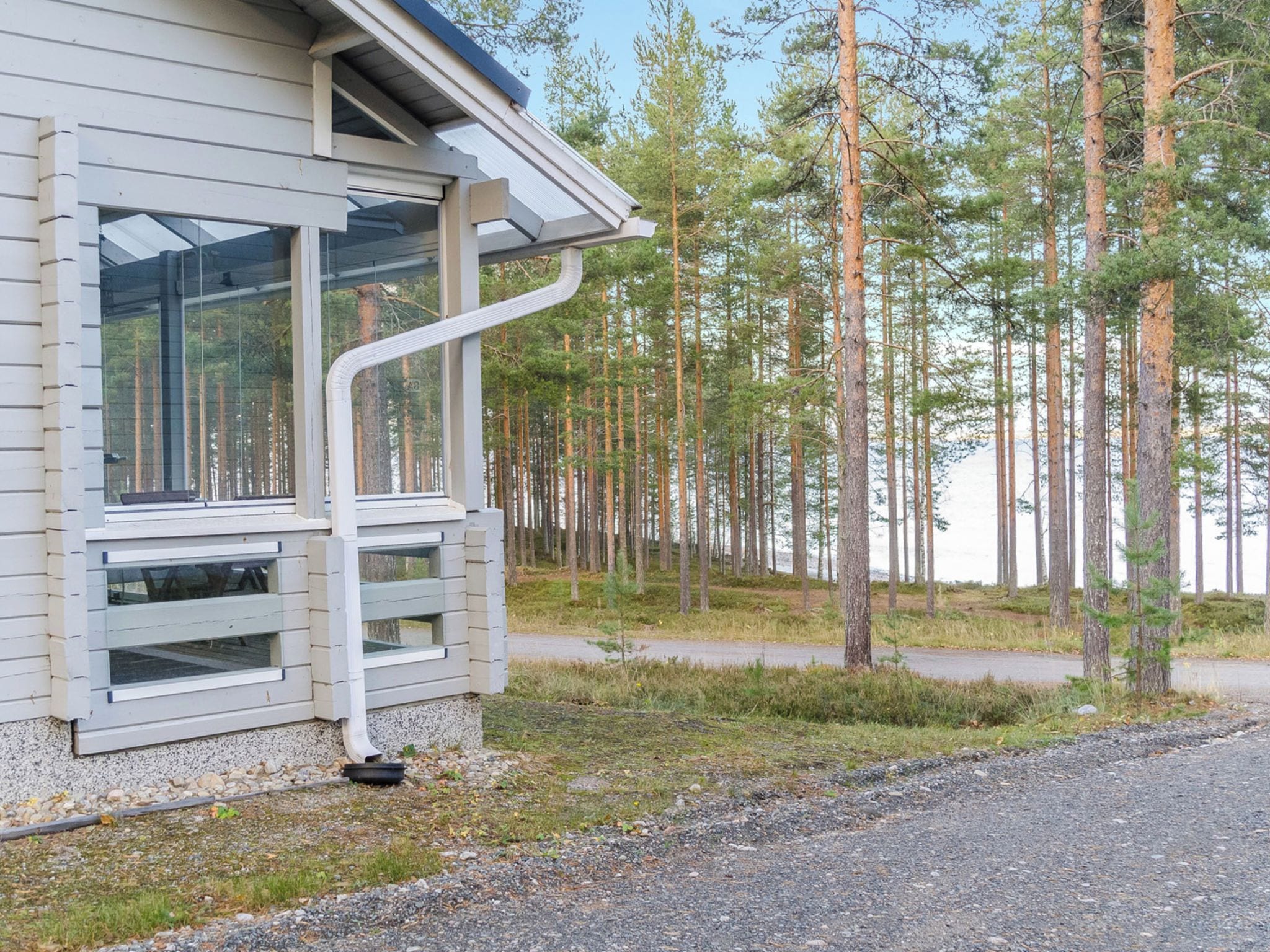 A modern building with large windows and a sloped roof, surrounded by a forest.