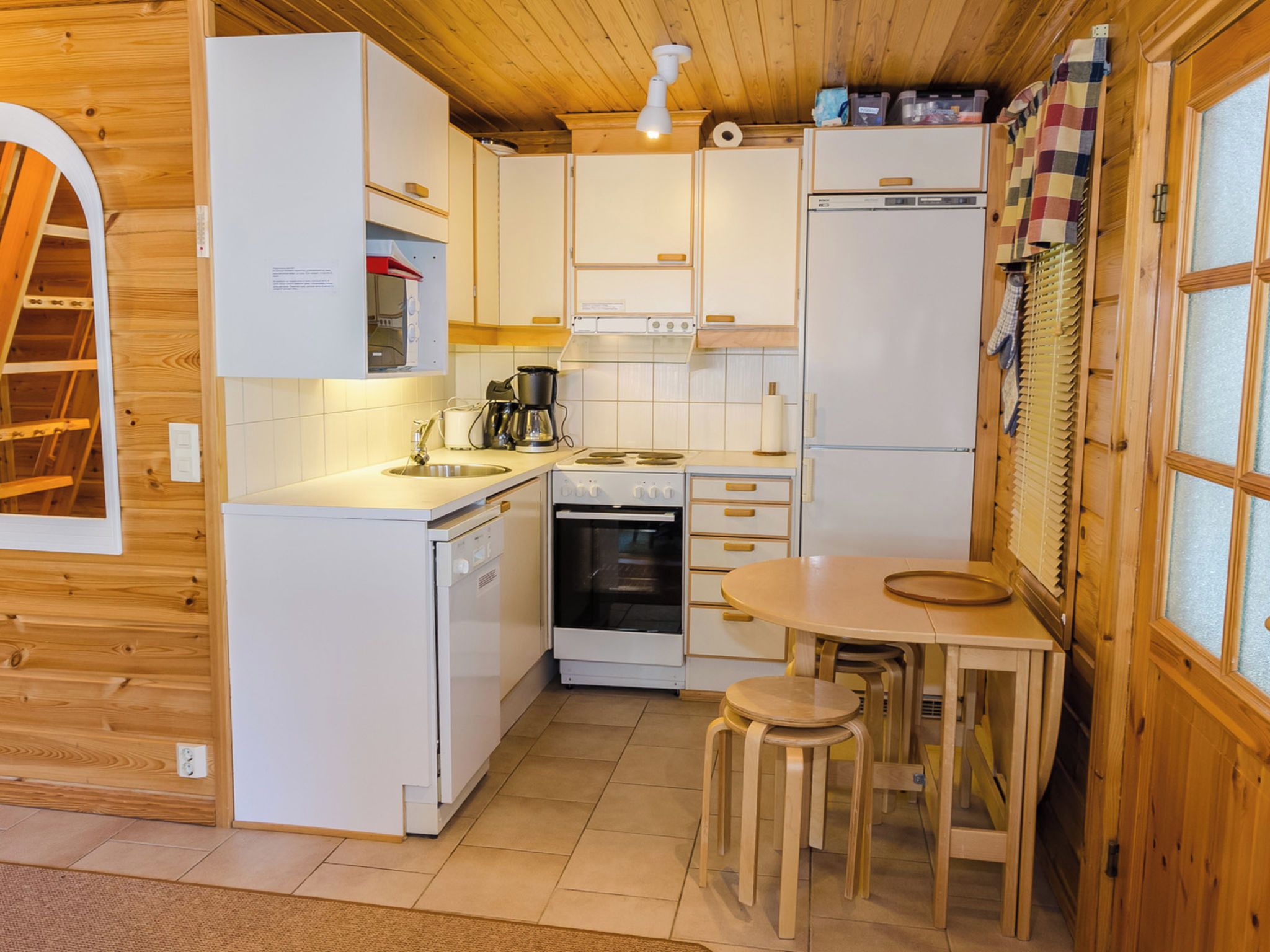 A compact kitchen with white cabinets, a stove, a sink, and a small dining area with stools.