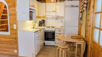A compact kitchen with white cabinets, a stove, a sink, and a small dining area with stools.