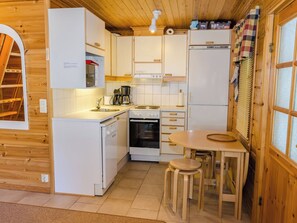 A compact kitchen with white cabinets, a stove, a sink, and a small dining area with stools.