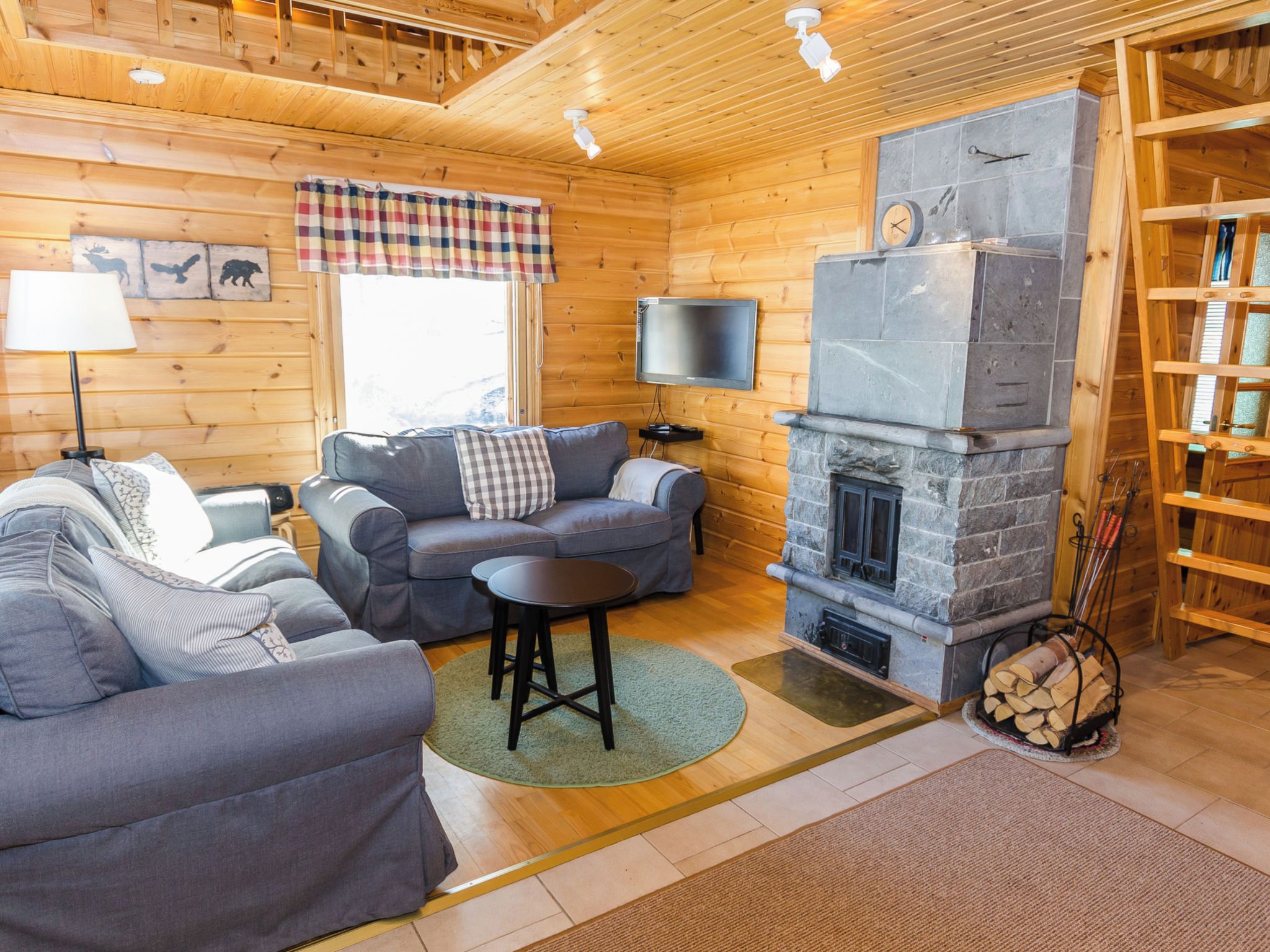A cozy cabin interior with a stone fireplace, wooden walls, a sofa, a television, and a bookshelf.