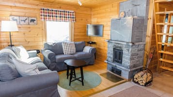A cozy cabin interior with a stone fireplace, wooden walls, a sofa, a television, and a bookshelf.