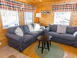 Et hyggeligt sommerrum med to grå sofaer, et lille rundt bord og ternede gardiner.