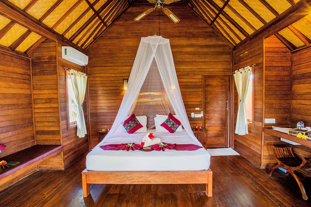 A wooden cabin room with a bed, a desk, and a chair.