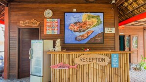 A reception desk with a wooden sign that reads "RECEPTION" and a "WELCOME" sign with a fish design. There is a clock, a map, and a sign indicating "FREE WIFI". - Pancali Cottages (Lembongan Island)