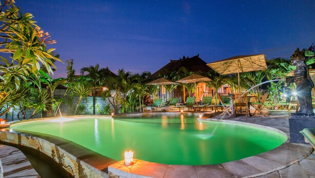 A nighttime pool area with lounge chairs and umbrellas, surrounded by tropical plants. - Pancali Cottages (Lembongan Island)