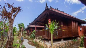 A traditional wooden building with a tiled roof, surrounded by a garden with various plants and a stone pathway. - Pancali Cottages (Lembongan Island)