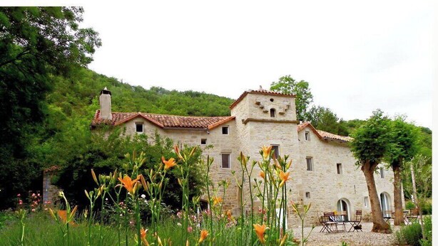 A stone building with a tower, surrounded by greenery and flowers.
