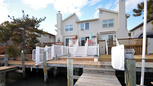A waterfront property with a dock, a wooden deck, and a two-story house with a balcony.