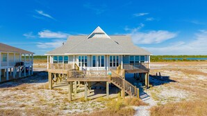 A beachfront house with a covered porch and a deck, surrounded by sand and sparse vegetation. - Beachfront | Pet Friendly | Gulf and Lagoon Views (Gulf Shores)