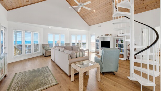 A spacious living room with a white staircase, wooden ceiling, and large windows. - Beachfront | Pet Friendly | Gulf and Lagoon Views (Gulf Shores)