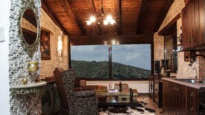 Une cuisine rustique avec un mur en pierre, un plafond en bois et une grande fenêtre donnant sur une colline.