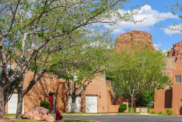 A residential area with stucco buildings, a large rock formation, and trees.