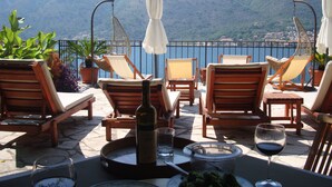 Una terraza con sillas de madera, una mesa de comedor con copas de vino, una botella de vino y un plato de comida.