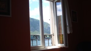 Una habitación con cama, ventana con vistas a un lago y montañas, y cortina en la ventana.