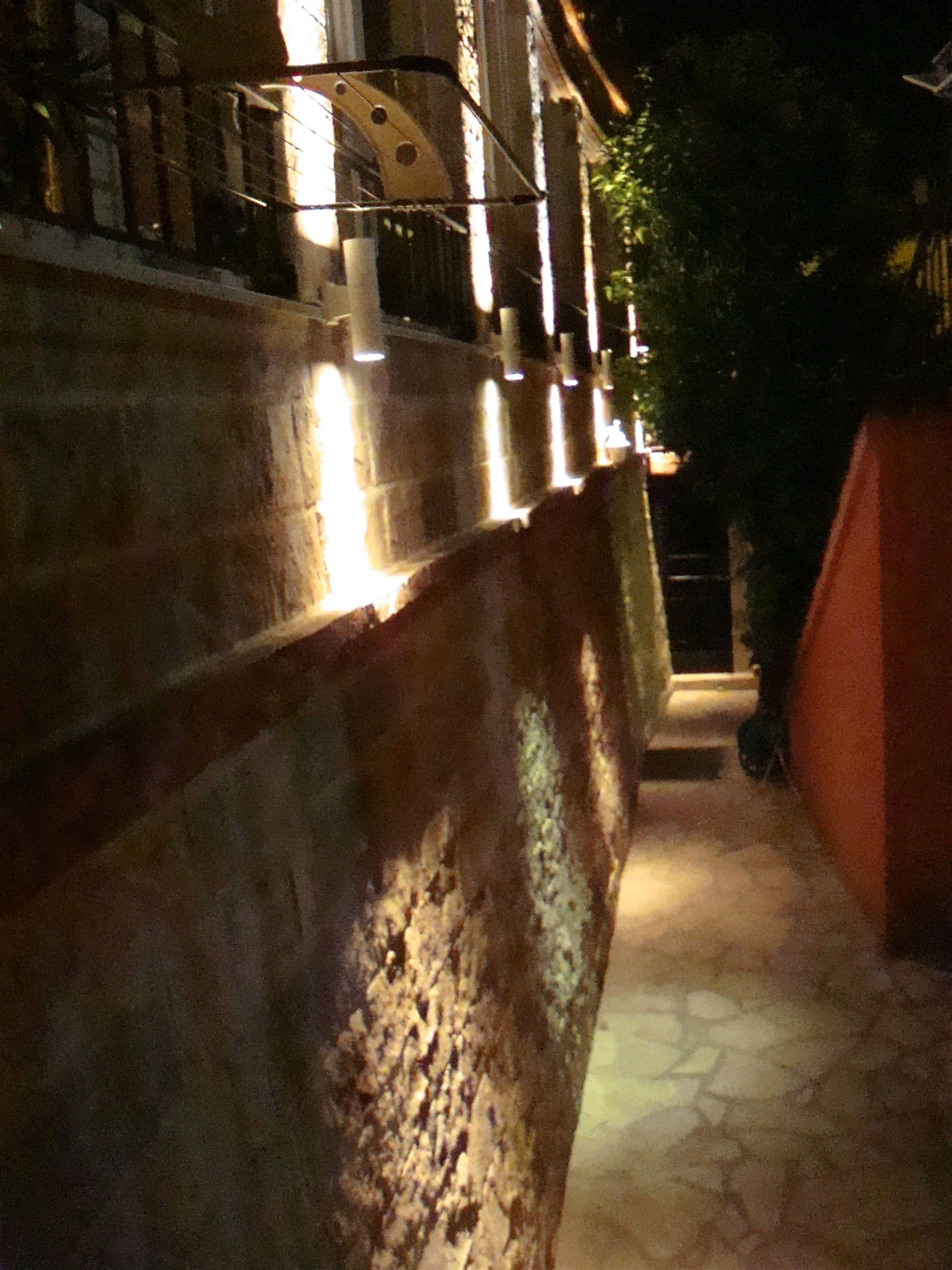 A stone pathway leading to a building with a metal railing and a red wall.