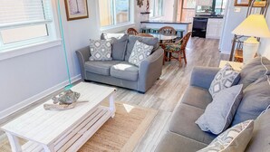 A cozy living room with a grey sofa, a wooden coffee table, and a dining area with a small table and chairs. - Inlet Point Villas #4C! Relax & Recharge in Cherry Grove’s Most Peaceful Corner (North Myrtle Beach)