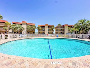 A swimming pool with a white fence, surrounded by multi-story buildings with red roofs. - Inlet Point Villas 4C (North Myrtle Beach)
