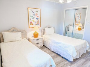 A bedroom with two beds, a nightstand with a lamp, a framed picture on the wall, and a mirror.