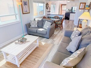 A living room with a sofa, a coffee table, and a dining area with chairs and a table. - Inlet Point Villas 4C (North Myrtle Beach)