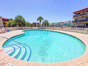 A round swimming pool with a tiled edge, surrounded by a wooden fence, and adjacent to multi-story buildings.