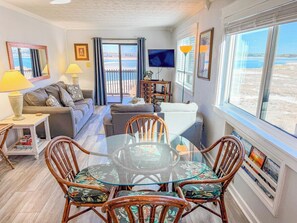 A living room with a glass table, wicker chairs, a sofa, a TV, and a view of the beach. - Inlet Point Villas 4C (North Myrtle Beach)