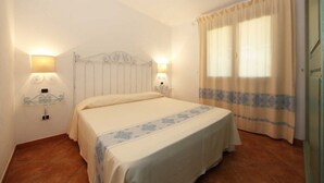 Un dormitorio con una cama, dos lámparas de pared, un ventanal con cortinas y una puerta.