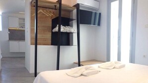 Habitació d'hotel amb llit, prestatge de fusta amb tovalloles i una cuineta al fons.
