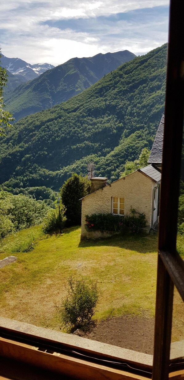 A rustic house with a sloped roof, surrounded by lush green hills and mountains.