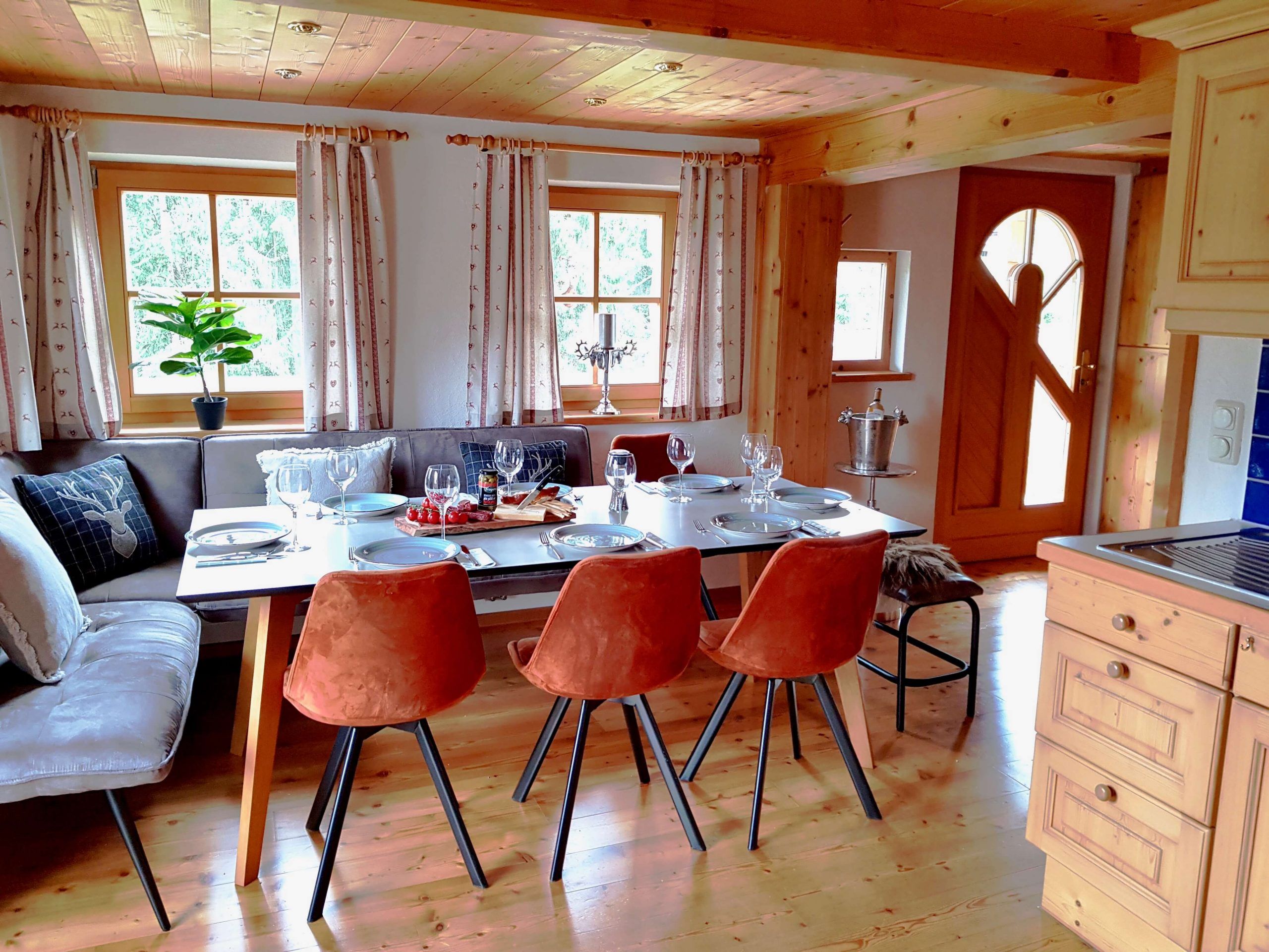 A dining area with a wooden table set for four, a sofa, and a kitchen area with wooden cabinets.