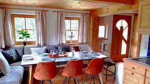 Uma sala de jantar com uma mesa de madeira posta para quatro lugares, um sofá e uma área de cozinha com armários de madeira.