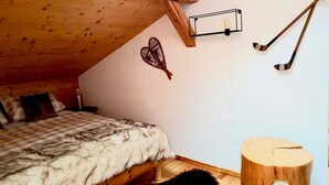 Quarto com teto inclinado, cama com coberta xadrez, cabeceira de madeira, luminária fixada na parede e tacos de hóquei na parede.