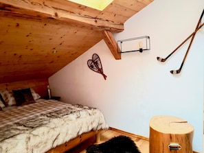 Un dormitorio con techo inclinado, una cama con manta a cuadros, cabecera de madera, lámpara de pared y palos de hockey en la pared.