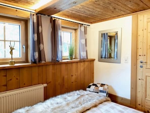 A bedroom with wooden paneling, a radiator, a bed with a fur throw, a window with curtains, and a mirror on the wall.