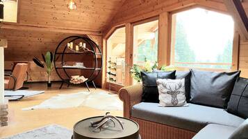 Un intérieur chaleureux en bois, avec un canapé, une table ronde, une bibliothèque et une grande fenêtre.