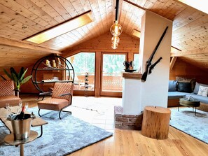 A cozy attic room with wooden beams, a loft bed, a dining area, and a view of the outdoors.
