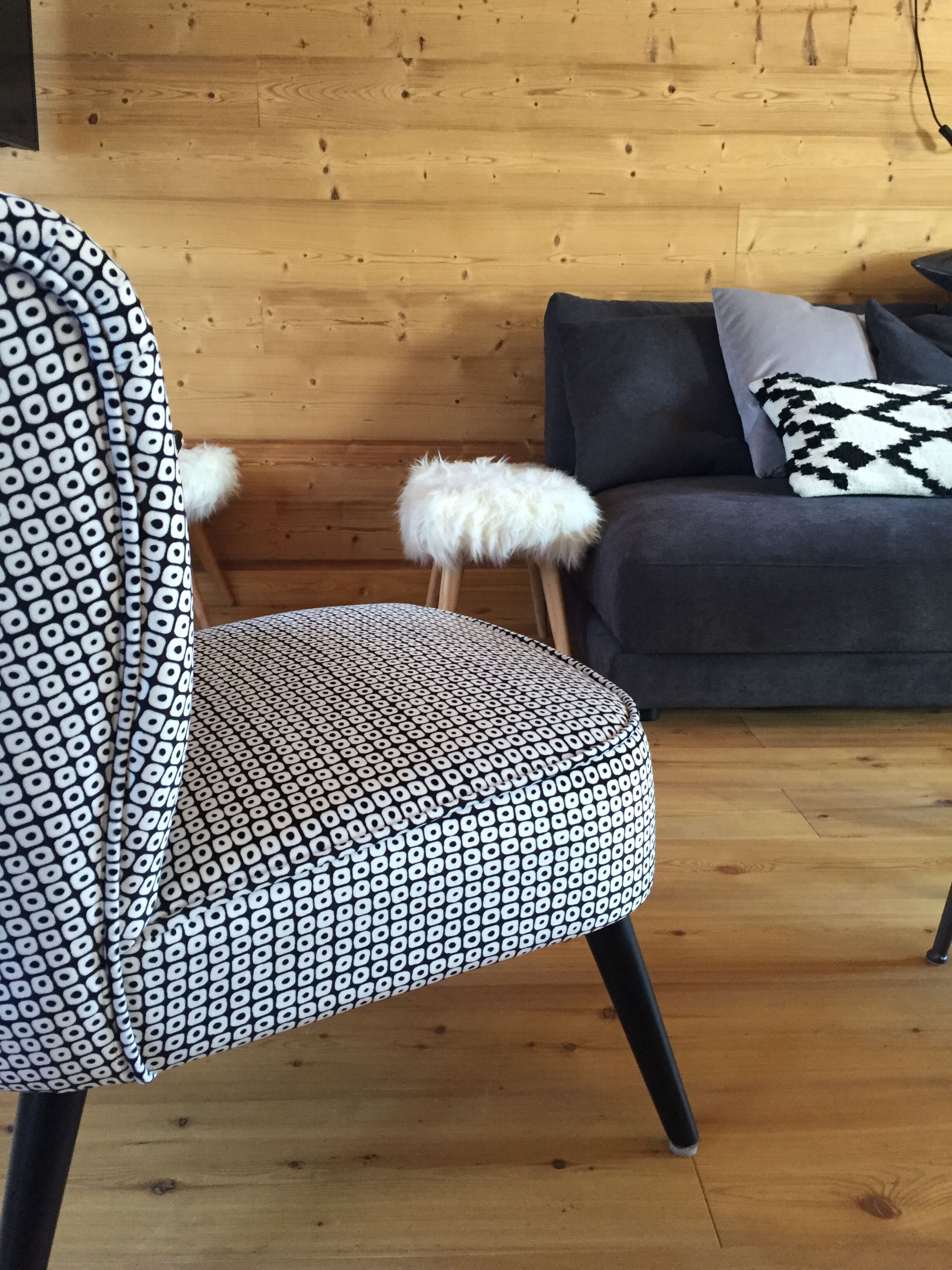 A modern living room with a patterned armchair, a fluffy white pouf, and a grey sofa with patterned cushions.
