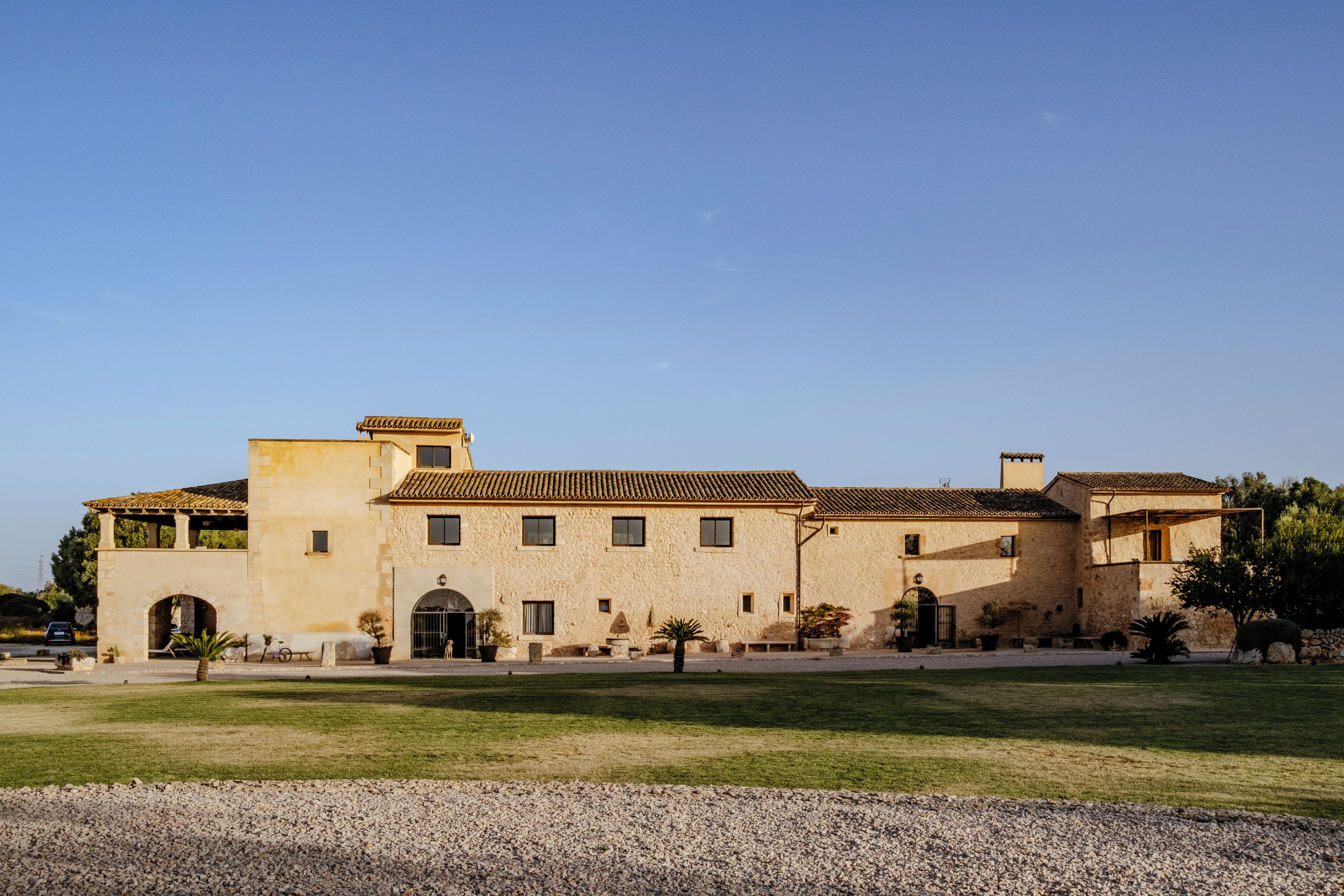 A large, single-story building with a tiled roof, multiple windows, and a paved courtyard.