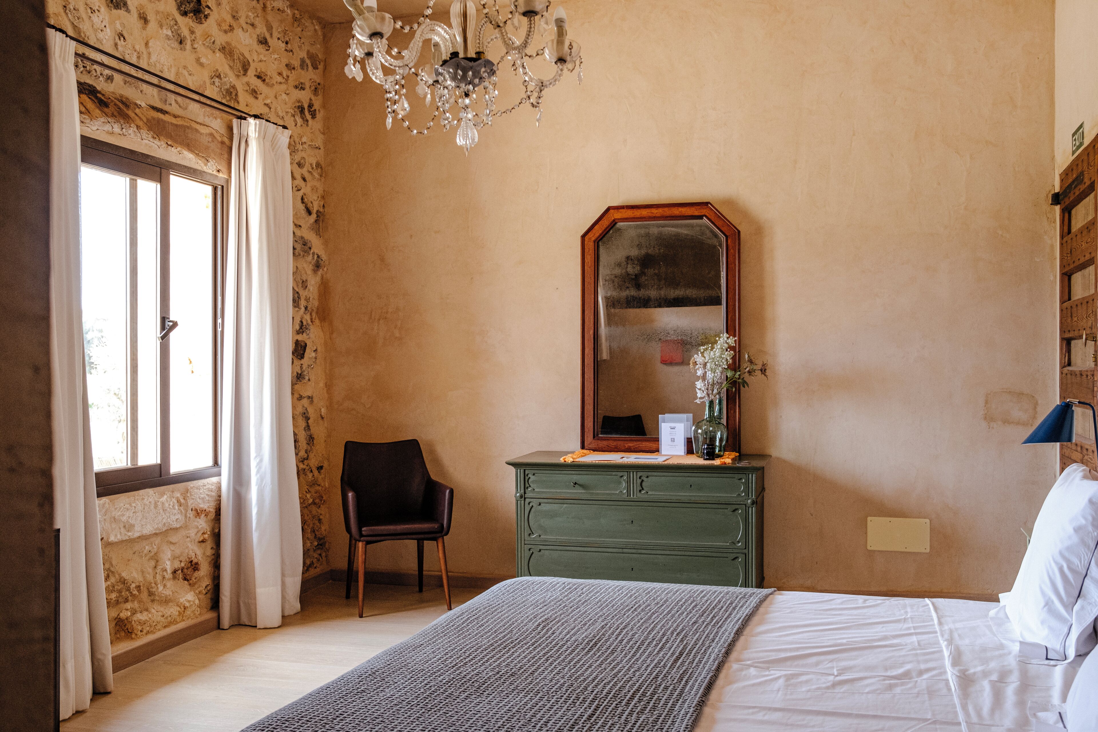 A bedroom with a bed, a dresser, a chair, a mirror, and a chandelier.