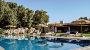A swimming pool with lounge chairs and umbrellas, a stone wall, and a building with a tiled roof. - Finca Gomera, Luxury Country House (Llucmajor)
