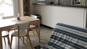 A compact room with a bed, a dining table with chairs, a kitchenette, and a window. - La Luciole – 3★ bright & comfortable apartment by the sea (ronce les bain)