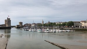 A harbor with numerous boats docked, a prominent tower, and a cityscape in the background. - La Luciole – 3★ bright & comfortable apartment by the sea (ronce les bain)