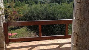 A balcony with a stone wall and a wooden railing overlooking a lush green landscape with hills in the distance. - Charming house near the sea South Corsica (Sollacaro)