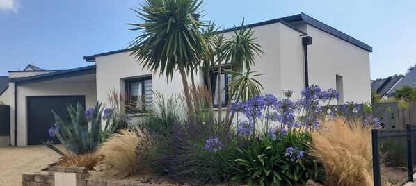 A modern two-story house with a garage, surrounded by a variety of plants and flowers.