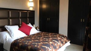 Une chambre d’hôtel avec un grand lit, une tête de lit, deux armoires et un luminaire fixé au mur.