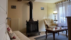 Ein Wohnzimmer mit einem schwarzen Kaminofen, einem beigen Sofa, einem cremefarbenen Sessel und einem Holztisch.